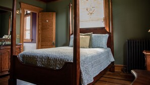 Una cama con dosel sobre pilares de madera, un aparador de madera con espejo y un radiador en el suelo.