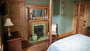 Una habitación con suelo de madera, chimenea, una silla y una cama.