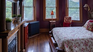 A bedroom with a wooden bed, a nightstand, a radiator, and a window with blinds.