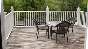 A wooden deck with wicker chairs and a table, surrounded by a white railing.