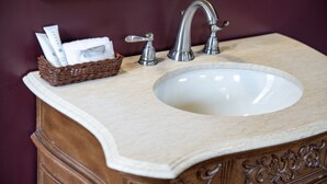A bathroom with a marble sink, a wooden cabinet, and a wicker basket with toiletries.