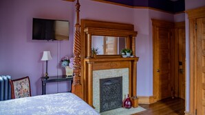 A bedroom with a four-poster bed, a fireplace, a television mounted on the wall, and a wooden door.
