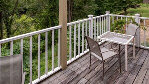 A wooden deck with a white railing, a glass table, and two chairs.