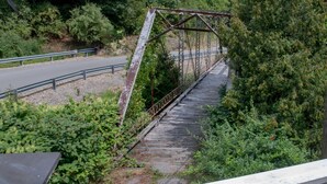Un puente de metal con pasarela de madera, rodeado de abundante vegetación.