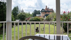A covered patio with a glass table and chairs, overlooking a well-maintained lawn and a brick house with a green roof.