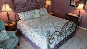 Un dormitorio con una cama, dos mesitas de noche, una silla y un espejo en la pared.