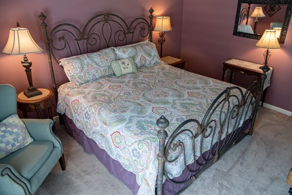 A bedroom with a bed, two bedside tables, a chair, and a mirror on the wall.