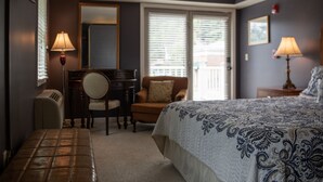 A hotel room with a bed, a desk, a chair, a lamp, and a window with blinds.