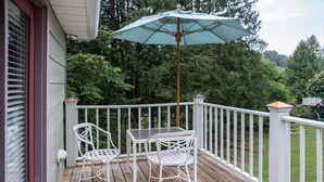 A wooden deck with two white metal chairs and a table, an umbrella, and a white railing.