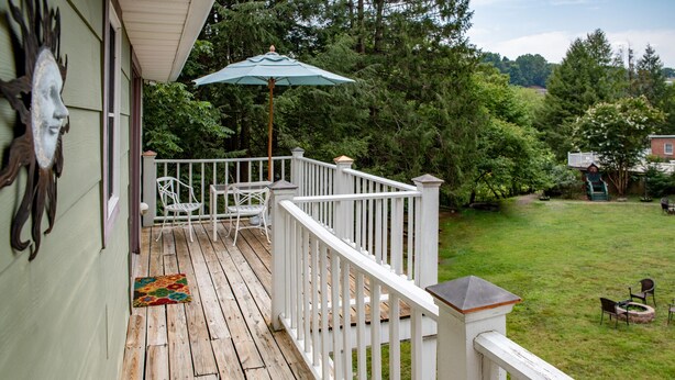 A wooden deck with white railings, a green umbrella, and a decorative wall piece.