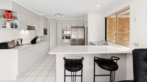 A modern kitchen with white cabinetry, a stainless steel refrigerator, and a large island with two black bar stools.