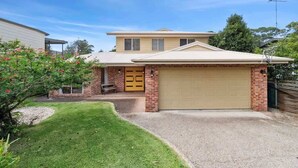 A two-story house with a garage, a front yard with a lawn and a small tree, and a brick driveway.