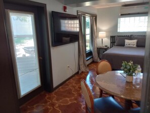 Una habitación con cama, televisión montada en la pared, mesa con sillas y ventana con cortinas.