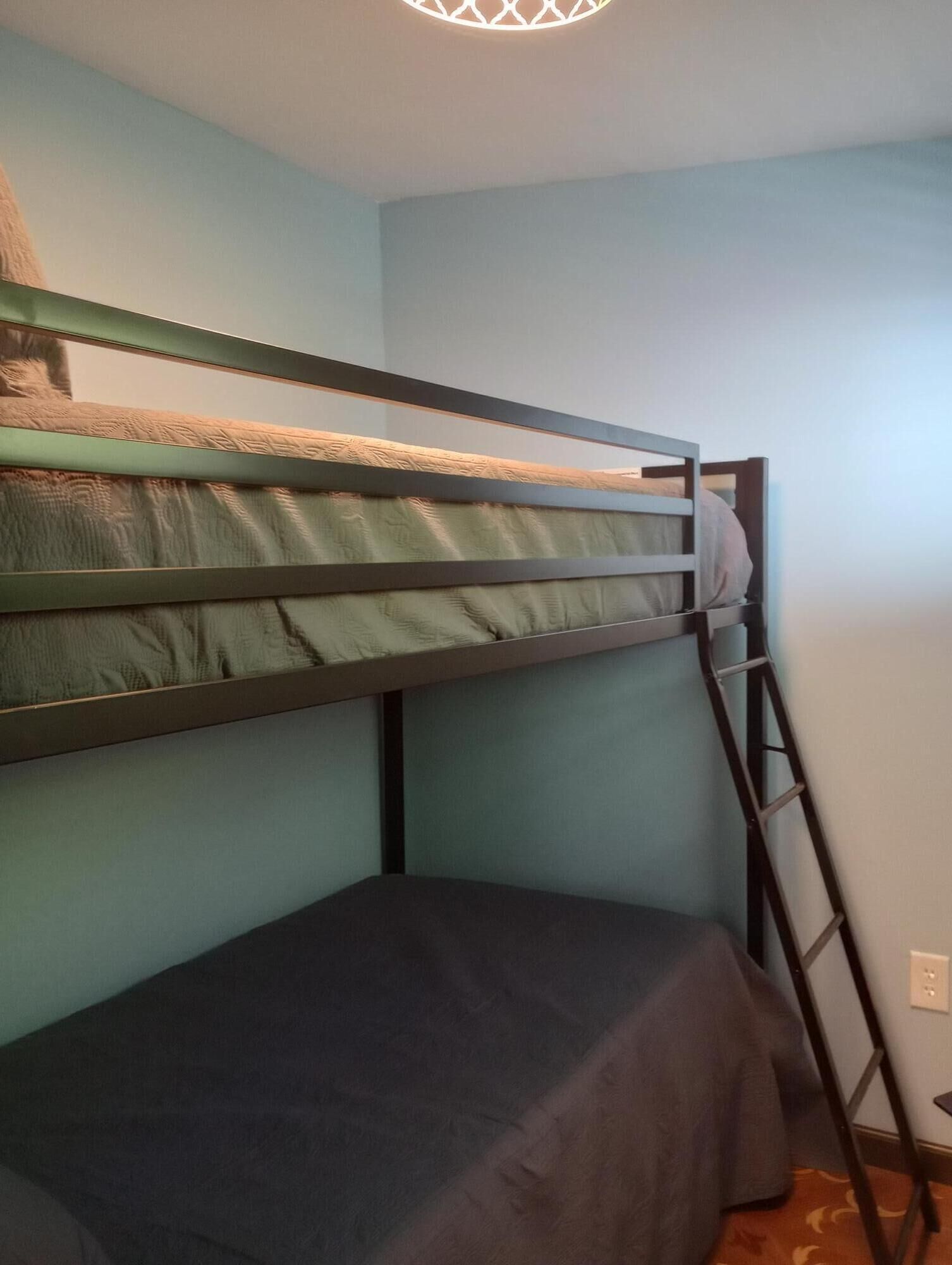 Ein Etagenbett mit einer Leiter, ein kleiner Tisch und eine schlichte Wand.