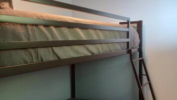 Una cama litera con escalera, una mesita pequeña y una pared lisa.