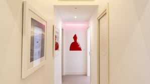 Un couloir avec des tableaux encadrés accrochés aux murs, une décoration murale représentant une silhouette rouge, et une porte sur la droite.
