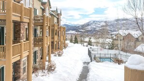 Un sentier enneigé mène à un espace piscine d’où l’on peut admirer la vue sur les montagnes et un immeuble résidentiel doté de balcons.