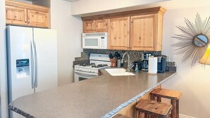 Une cuisine avec des meubles en bois, un plan de travail en granit, un réfrigérateur, un four à micro-ondes, une cuisinière et un évier.