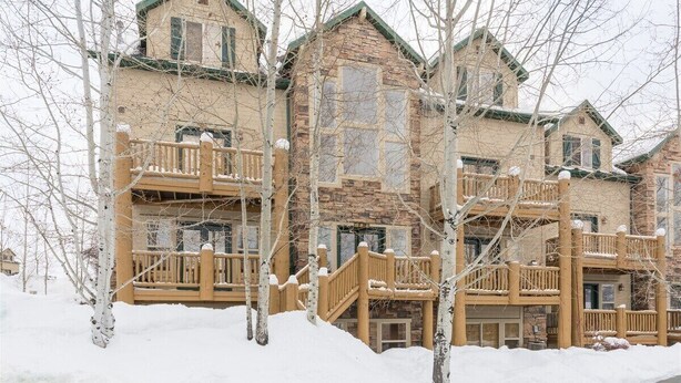 Un chalet à étages doté de balcons en bois et d’une façade en pierre, entouré d’arbres couverts de neige.