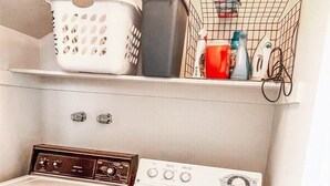 Un espace buanderie comprenant un lave-linge, un sèche-linge et des étagères où sont rangés les paniers à linge et les produits de nettoyage.