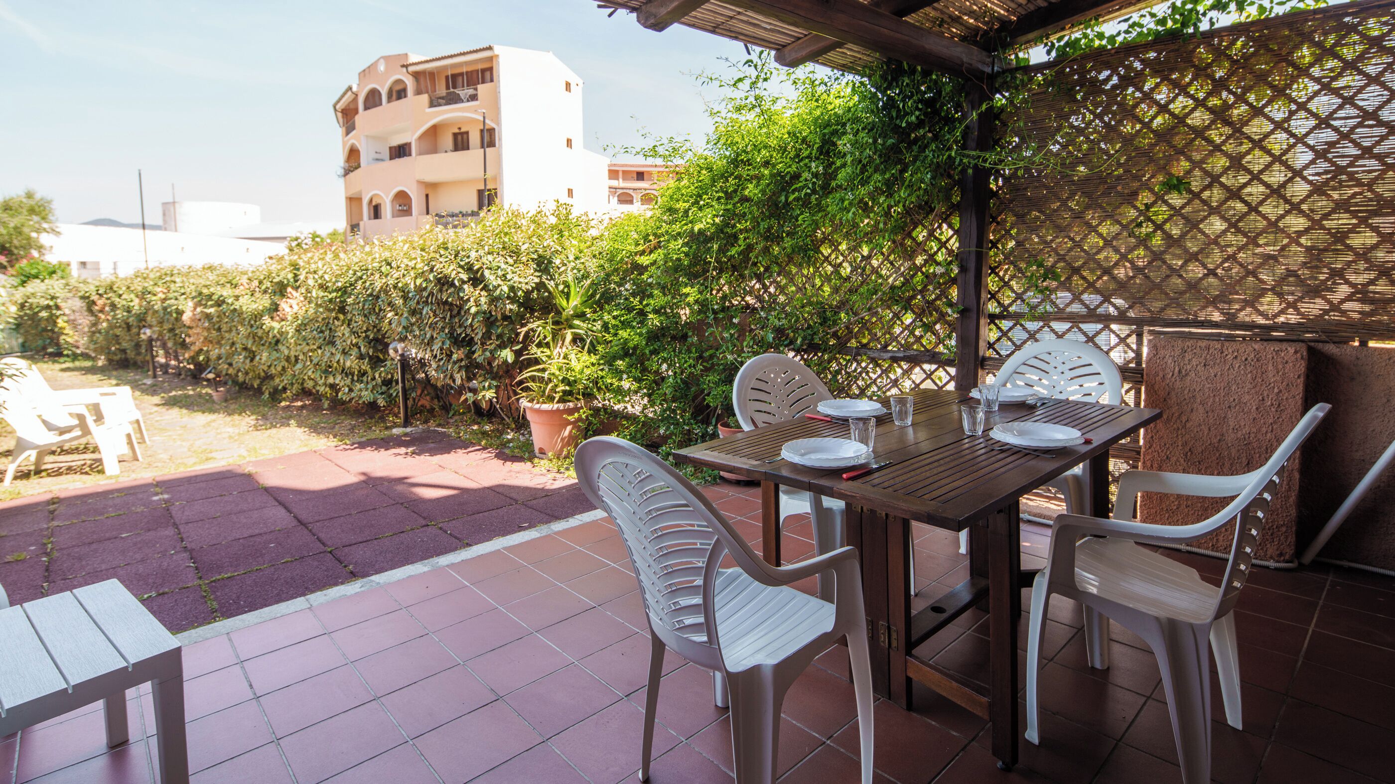 Terrassa a l'aire lliure amb taula preparada per dinar, rodejada de cadires i una vista d'un edifici al fons.