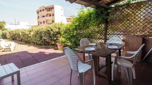 Une terrasse extérieure avec une table dressée pour le repas, entourée de chaises, et une vue sur un bâtiment en arrière-plan.