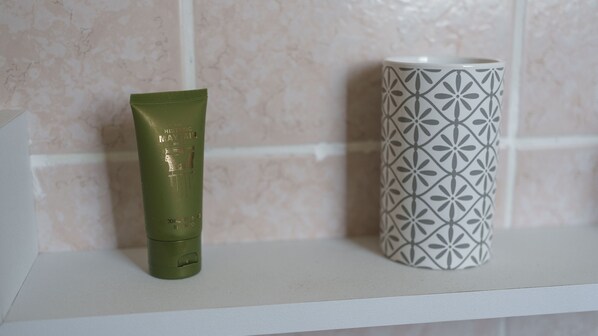 Un tubo verde y una taza con estampado sobre una estantería blanca.