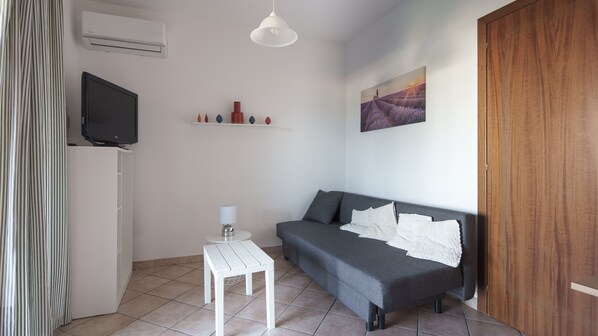 Une petite pièce moderne, avec un canapé gris, une table blanche, un téléviseur, un tableau et une armoire en bois.