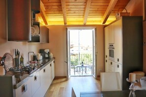 A compact kitchen with wooden beams, a central island, and a sliding glass door leading to an outdoor patio. - Civico Sei (Menaggio)