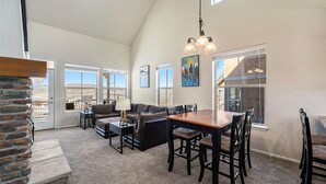 Un salón amplio con chimenea, un comedor con mesa y sillas de madera, y ventanas grandes que ofrecen vistas al exterior.