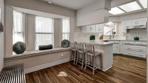 A modern kitchen with white cabinetry, a central island with bar stools, and large windows with sheer curtains. - Luxury rental in Southlake on 1-Acre! (Southlake)