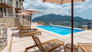 Ein Poolbereich mit Liegestühlen und Sonnenschirmen, ein Steinhaus und eine Bergblick.