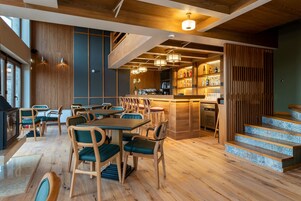 A restaurant with wooden floors, green upholstered chairs, and a bar area with a staircase.
