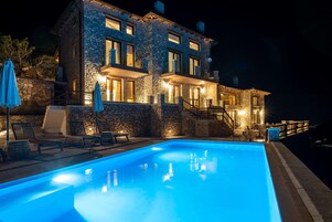A stone building with a swimming pool, outdoor seating, and a staircase leading to the upper floors.