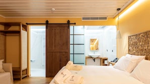 Ein Hotelzimmer mit einem großen Bett, einem Holzschrank, einer Schiebetür, einem kleinen Nachttisch mit Lampe und einem durch die Tür einsehbaren Badezimmer.