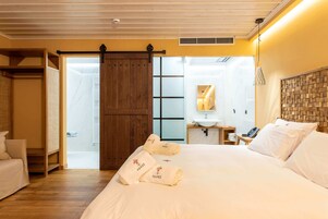 A hotel room with a large bed, a wooden wardrobe, a sliding door, a small bedside table with a lamp, and a bathroom visible through the door.