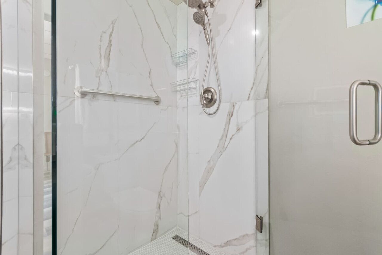 Une douche fermée par des parois de verre, avec un mur en marbre, une barre d’appui et un pommeau de douche.