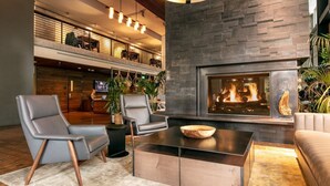 Un'area lounge moderna con poltrone in pelle, un camino e una sala da pranzo con soffitto alto e travi a vista.