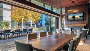 A modern conference room with a large wooden table, comfortable seating, a fireplace, and a large TV screen. - Luxury Living: 2BR Condo at Via 6 (Seattle)