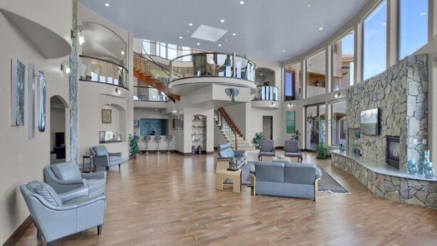 A spacious living area with a high ceiling, a central staircase, and a stone fireplace. - Luxury Mansion Retreat, Sleeps 16+ ,Panoramic VIEWS 36 Acre Land .in the city . (Castle Rock)