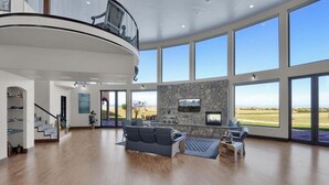 A spacious living area with a stone fireplace, large windows, and a modern staircase. - Luxury Mansion Retreat, Sleeps 16+ ,Panoramic VIEWS 36 Acre Land .in the city . (Castle Rock)