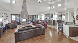 A spacious living area with a large sofa, a fireplace, and a kitchen in the background. - Luxury Mansion Retreat, Sleeps 16+ ,Panoramic VIEWS 36 Acre Land .in the city . (Castle Rock)