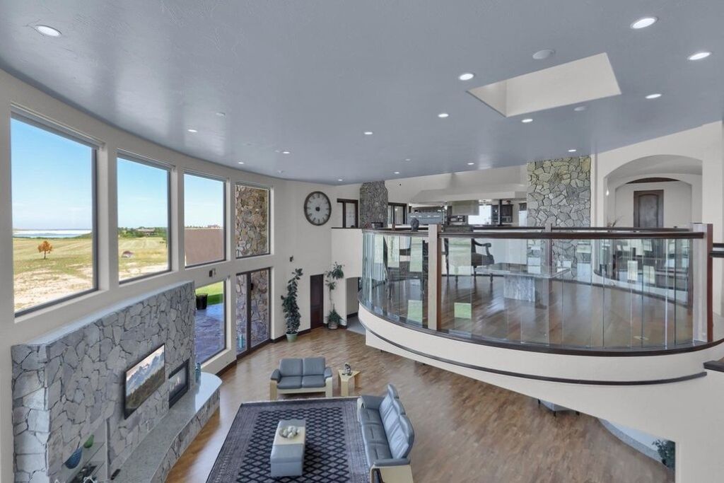A spacious living area with a stone fireplace, large windows, and a balcony with a glass railing.
