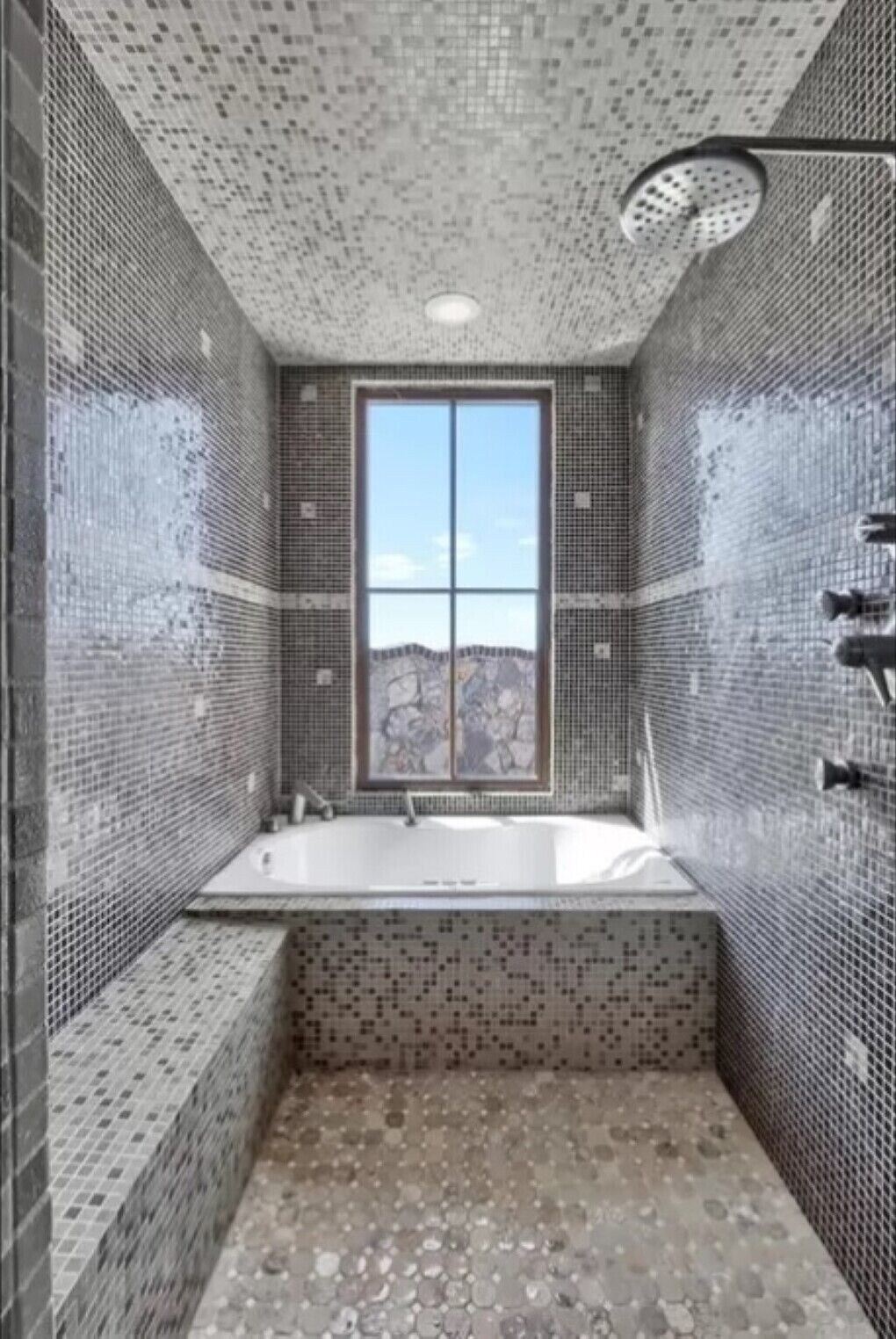 A bathroom with mosaic tile walls, a large window, and a bathtub.