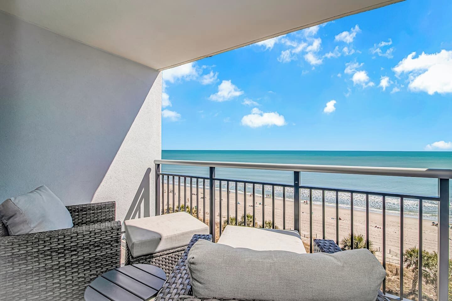 A balcony with wicker furniture, a view of the beach, and a clear sky.