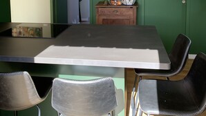 A dining area with a table and four chairs, a wooden cabinet with plants, and a door with a green wall. - Maison Contemporaine, Confortable et Lumineuse (Saint-Briac-sur-mer)
