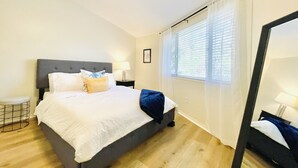 A bedroom with a bed, bedside tables, a ceiling fan, a window with curtains, and a mirror. - The Leia 2BR Bright Retreat by Velvet Ditch Villas (Oxford)