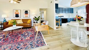 A modern living room with a brown leather sofa, a colorful rug, and a dining area with a white table and chairs. - The Leia 2BR Bright Retreat by Velvet Ditch Villas (Oxford)