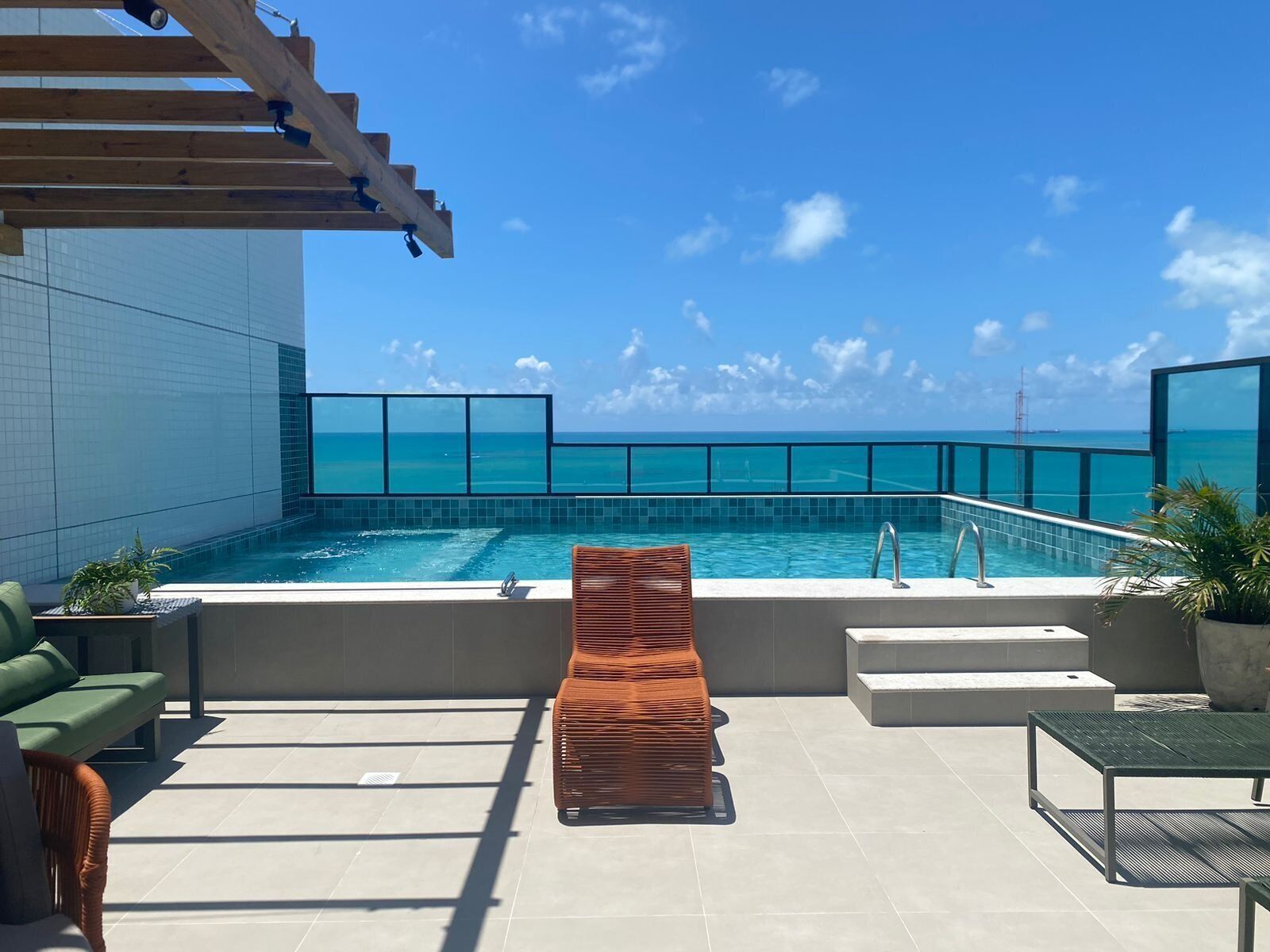 A rooftop pool with a clear view of the ocean, a lounge chair, and a green sofa.