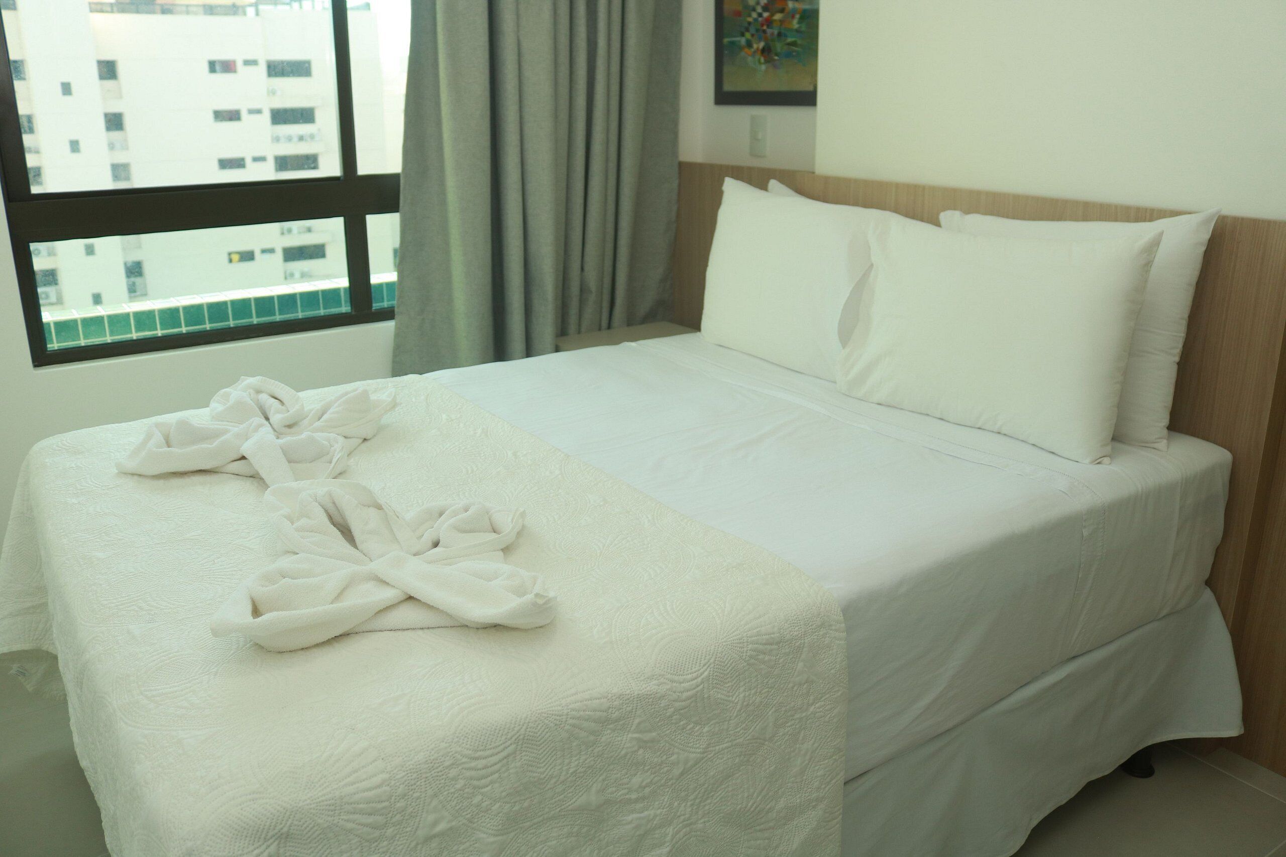 Una cama bien hecha con sábanas blancas y un par de batas de baño blancas sobre la cama.